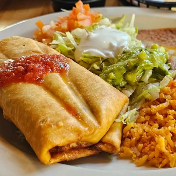 A golden-brown chimichanga topped with salsa, served with rice, guacamole, sour cream, and lettuce.