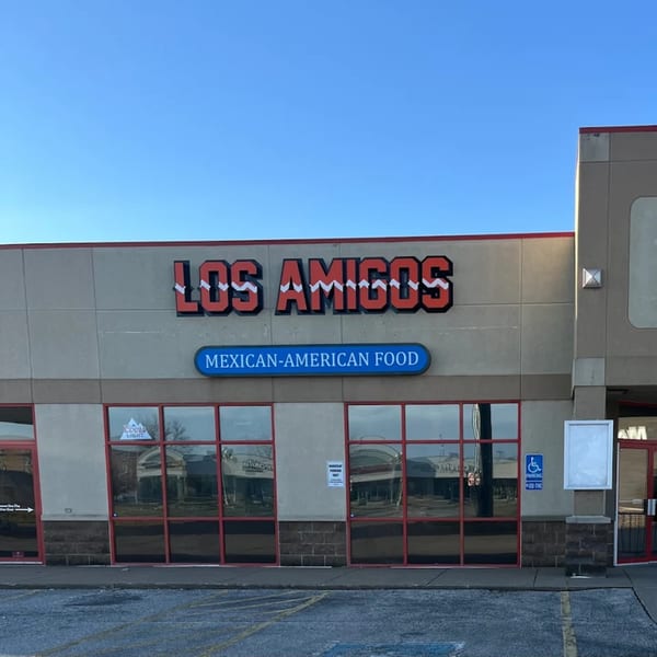 The exterior of Los Amigos restaurant, featuring its red and white sign and 'Mexican-American Food' banner.