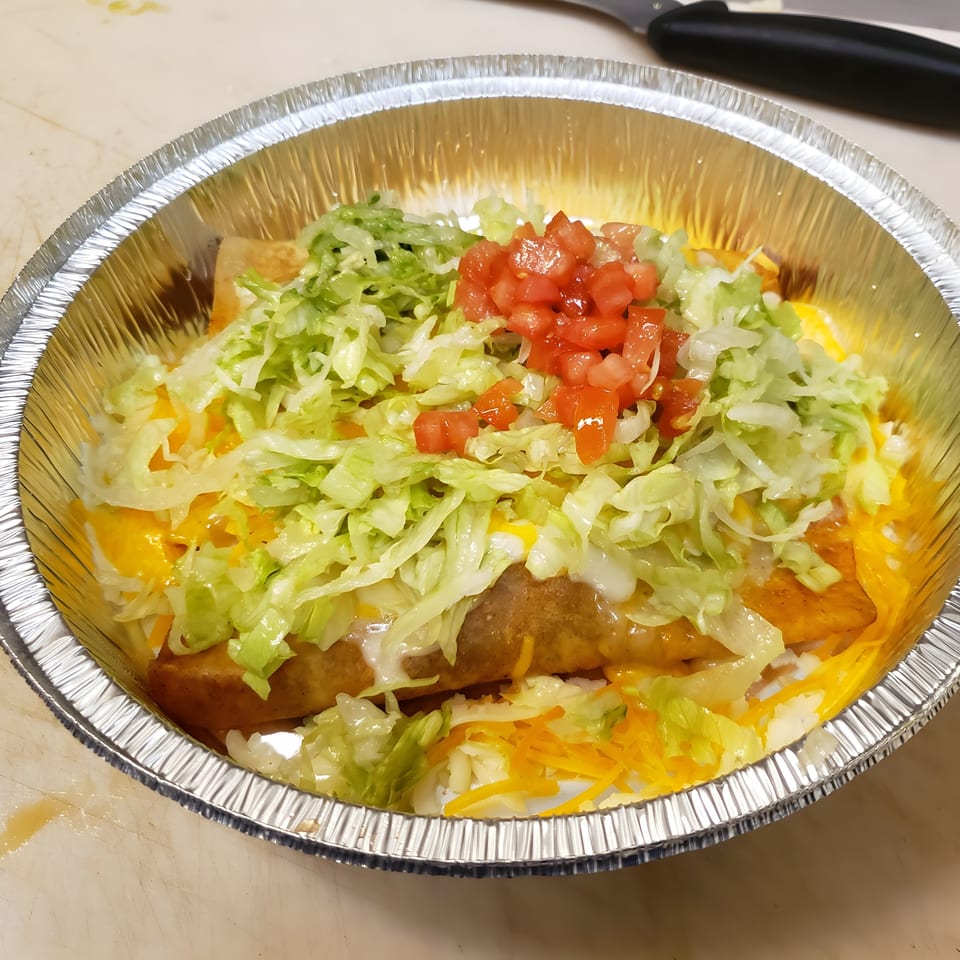 Los Amigos Mexican food in a foil container, topped with lettuce, tomatoes, and cheese.