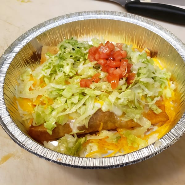 Los Amigos Mexican food in a foil container, topped with lettuce, diced tomatoes, and cheese.