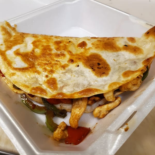 A golden-brown chicken fajita quesadilla with peppers and onions in a white takeout container.