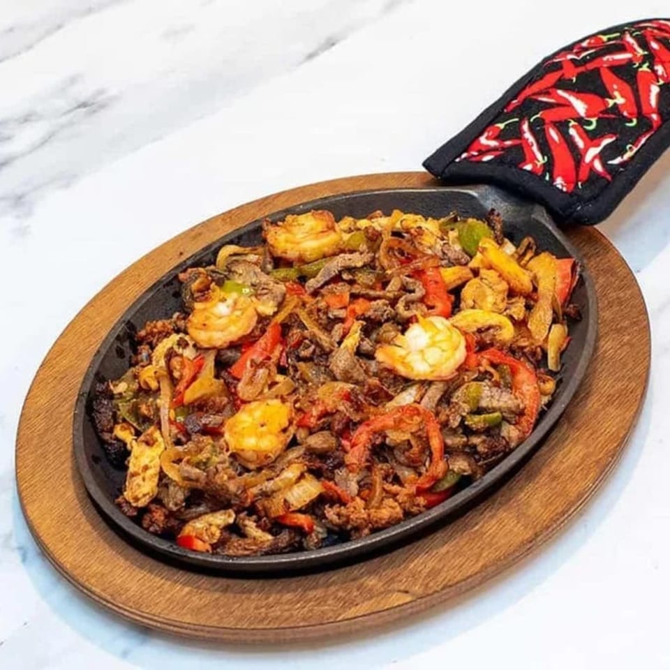 Sizzling Los Amigos fajitas with shrimp, beef, bell peppers, and onions in a cast-iron skillet.
