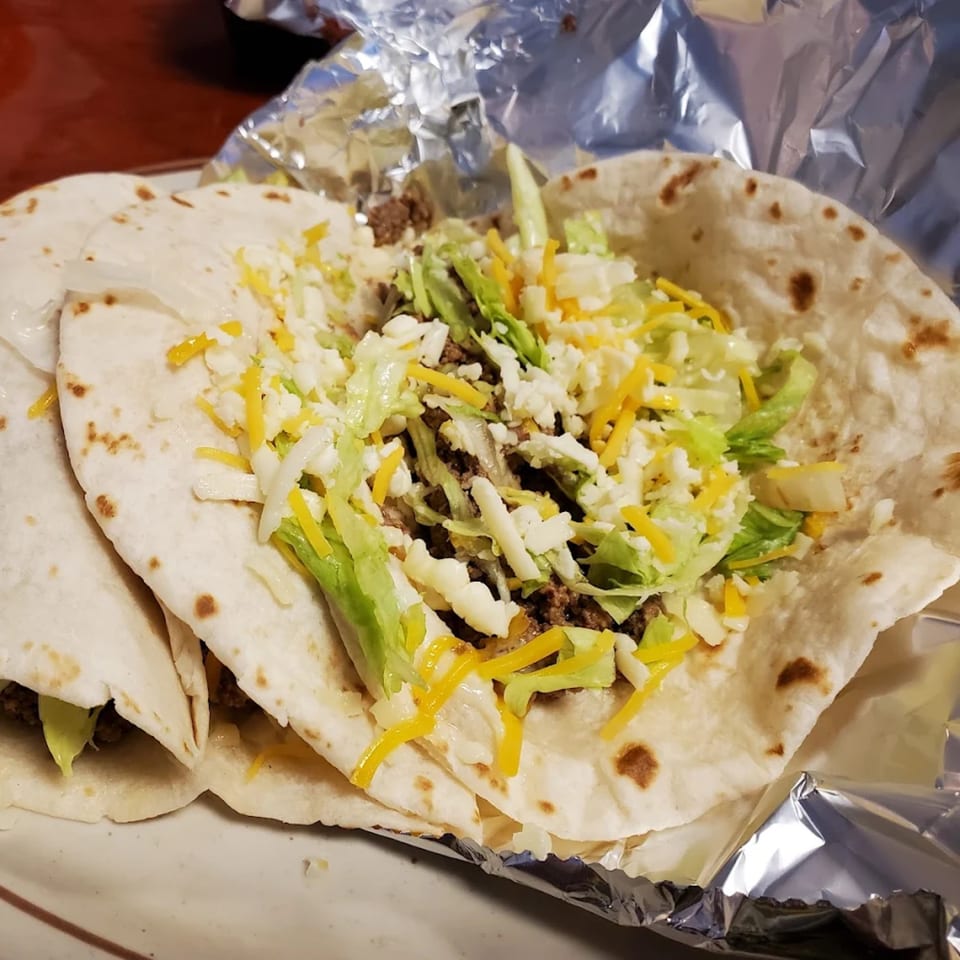 Two Los Amigos soft tacos filled with ground beef, shredded lettuce, and cheese, served in foil.