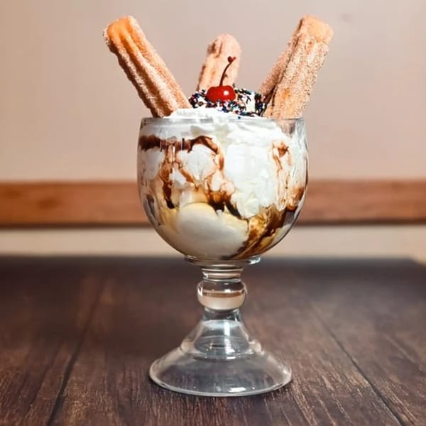 Churro sundae in a glass, topped with whipped cream, chocolate drizzle, sprinkles, and a cherry.