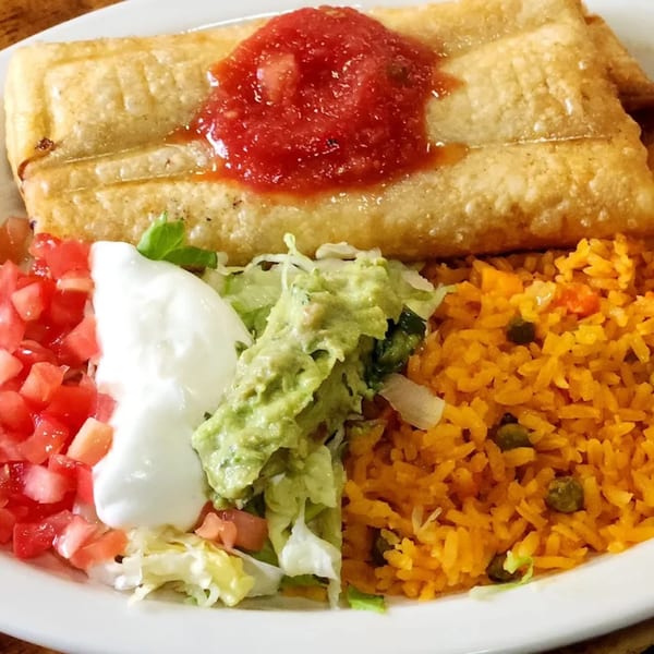 A golden-fried chimichanga topped with salsa, served with rice, guacamole, sour cream, and diced tomatoes.
